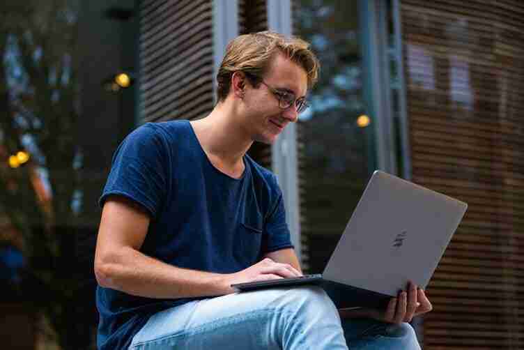 College student sitting on steps, absorbed in blogging on a laptop